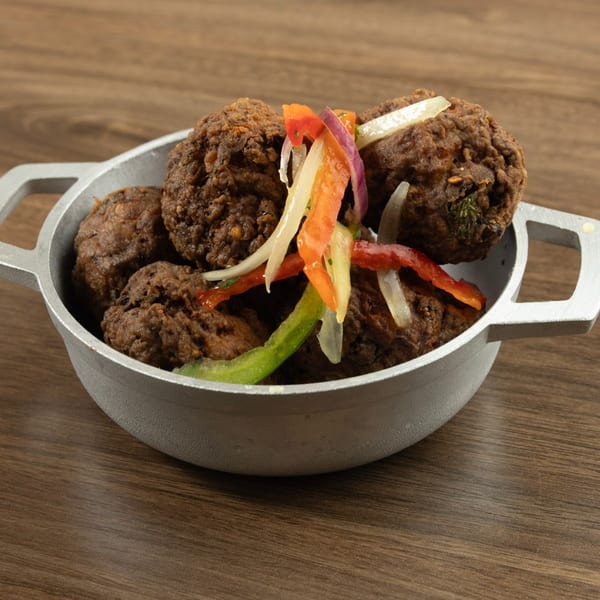 Haitian akra, fried malanga fritters, in a metal bowl, topped with colorful pickled vegetables.