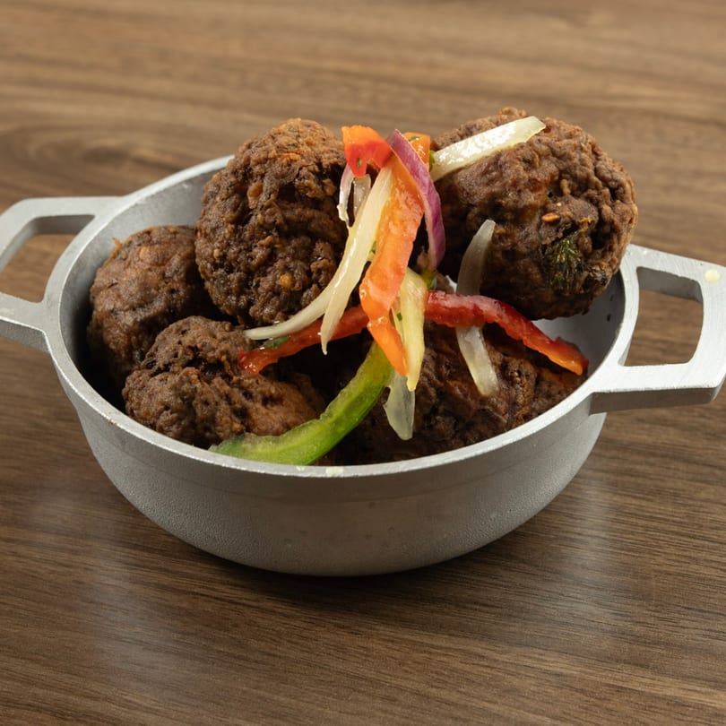 Haitian akra, fried malanga fritters, in a metal bowl, topped with colorful pickled vegetables.