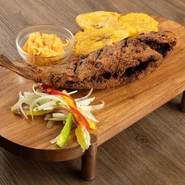 Haitian fried fish with plantains, pikliz, and a side of mango slaw on a wooden board.