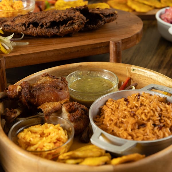 Haitian fried chicken, rice, plantains, and sauces served on a wooden platter.