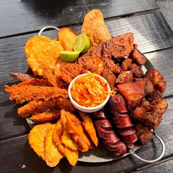 A large platter of Haitian fried foods, including plantains, sausage, pork, and a side of pikliz.