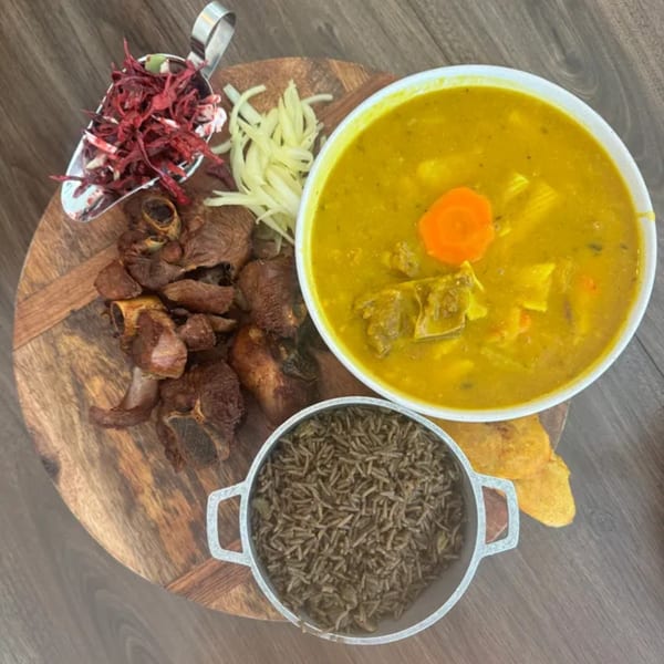 Haitian meal with fried meat, yellow soup, rice, and pickled vegetables on a wooden board.