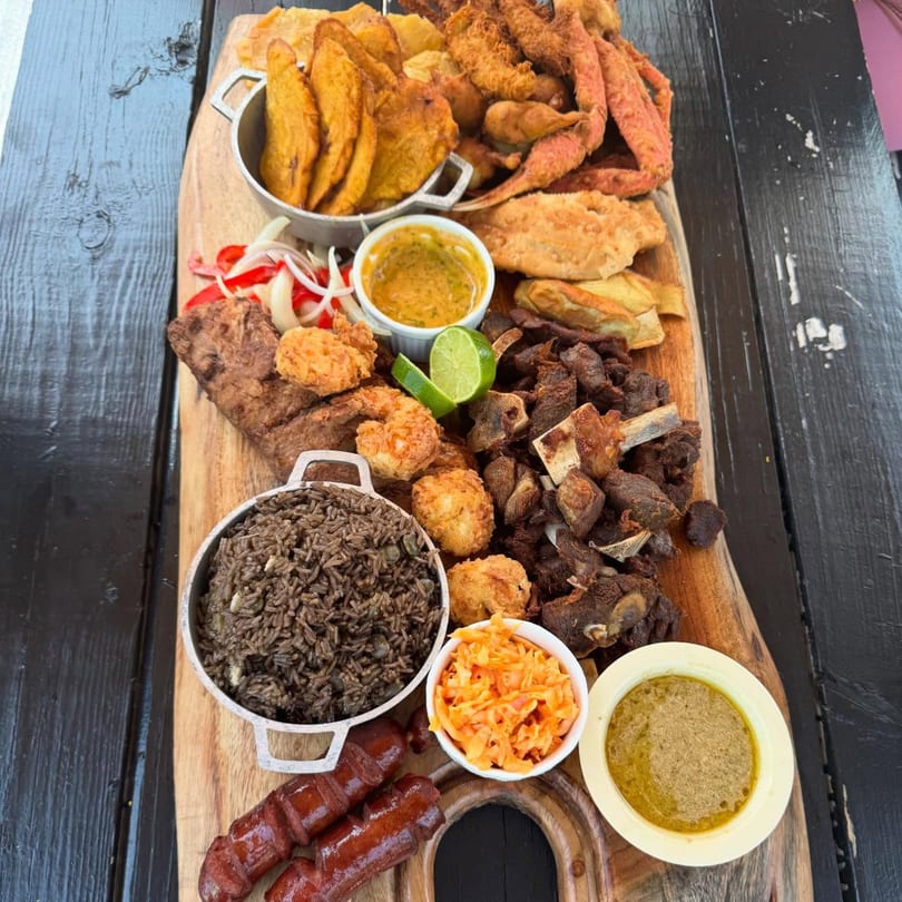 A large Haitian platter with fried plantains, crab, rice, fried pork, shrimp, and sauces.