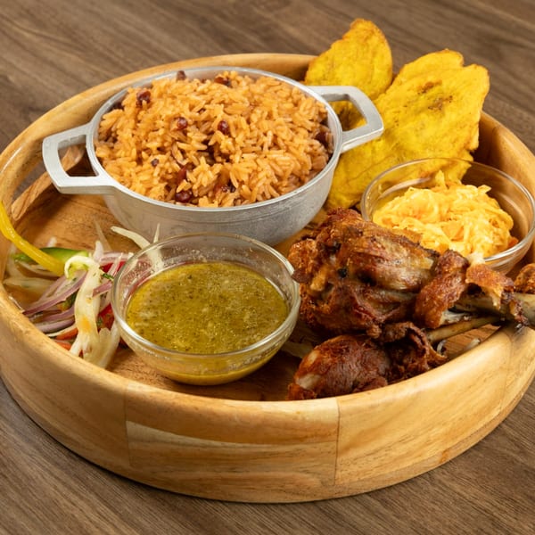 Haitian griot, rice and beans, plantains, pikliz, and sauce served on a wooden tray.