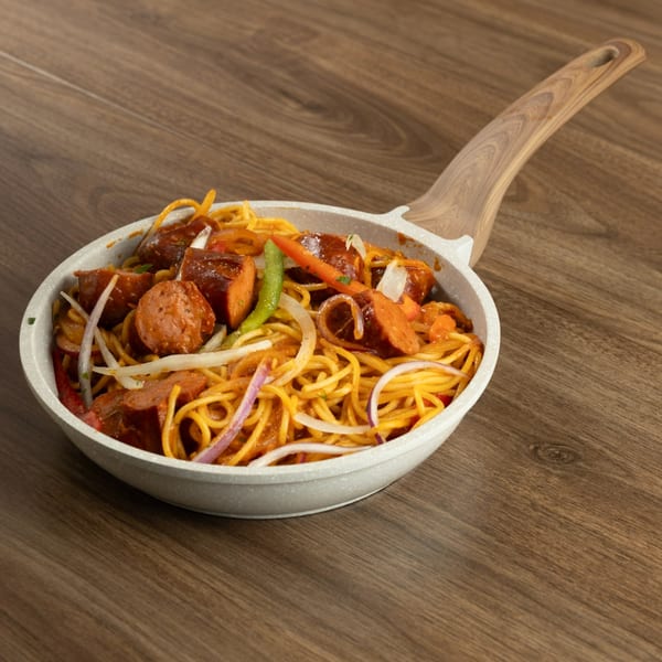 Haitian spaghetti with sausage, peppers, and onions in a white pan on a wooden table.