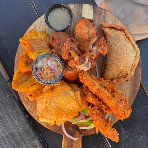 A Haitian platter with fried plantains, chicken, empanada, and other fried items with dipping sauces.